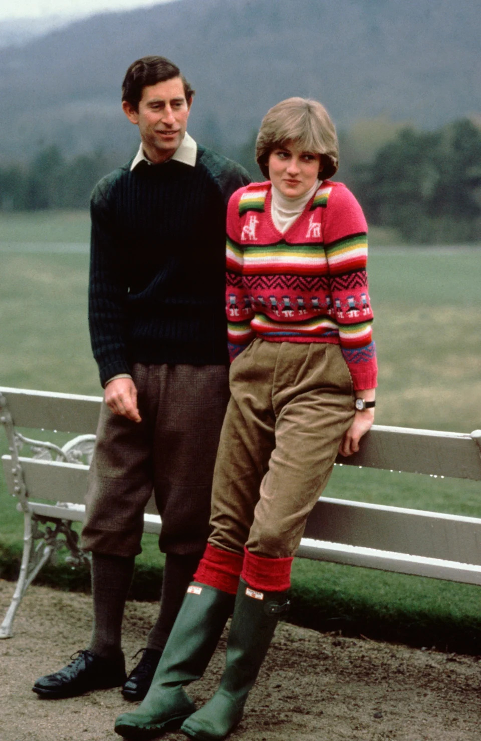 Prince Charles and Princess Diana leaning on a bench at Balmoral wearing sweaters
