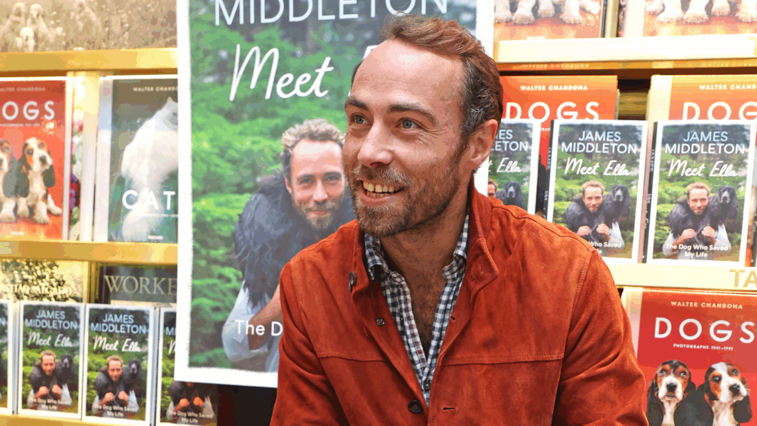 James Middleton sitting in front of a table of his memoir and bookshelves with dog books