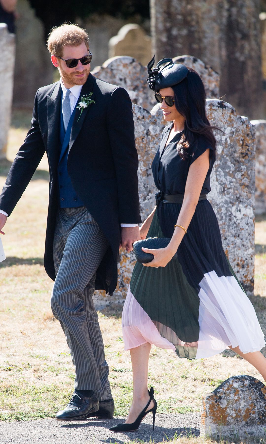 Prince Harry and Meghan Markle walk through a church yard, Prince Harry is wearing a formal suit and Meghan Markle is wearing a colour blocked midi dress and black high heels 
