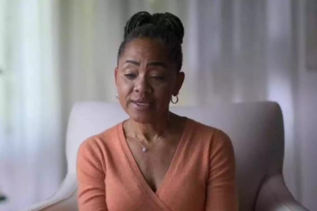 A woman sitting in a chair wearing an orange sweater and her hair up.
