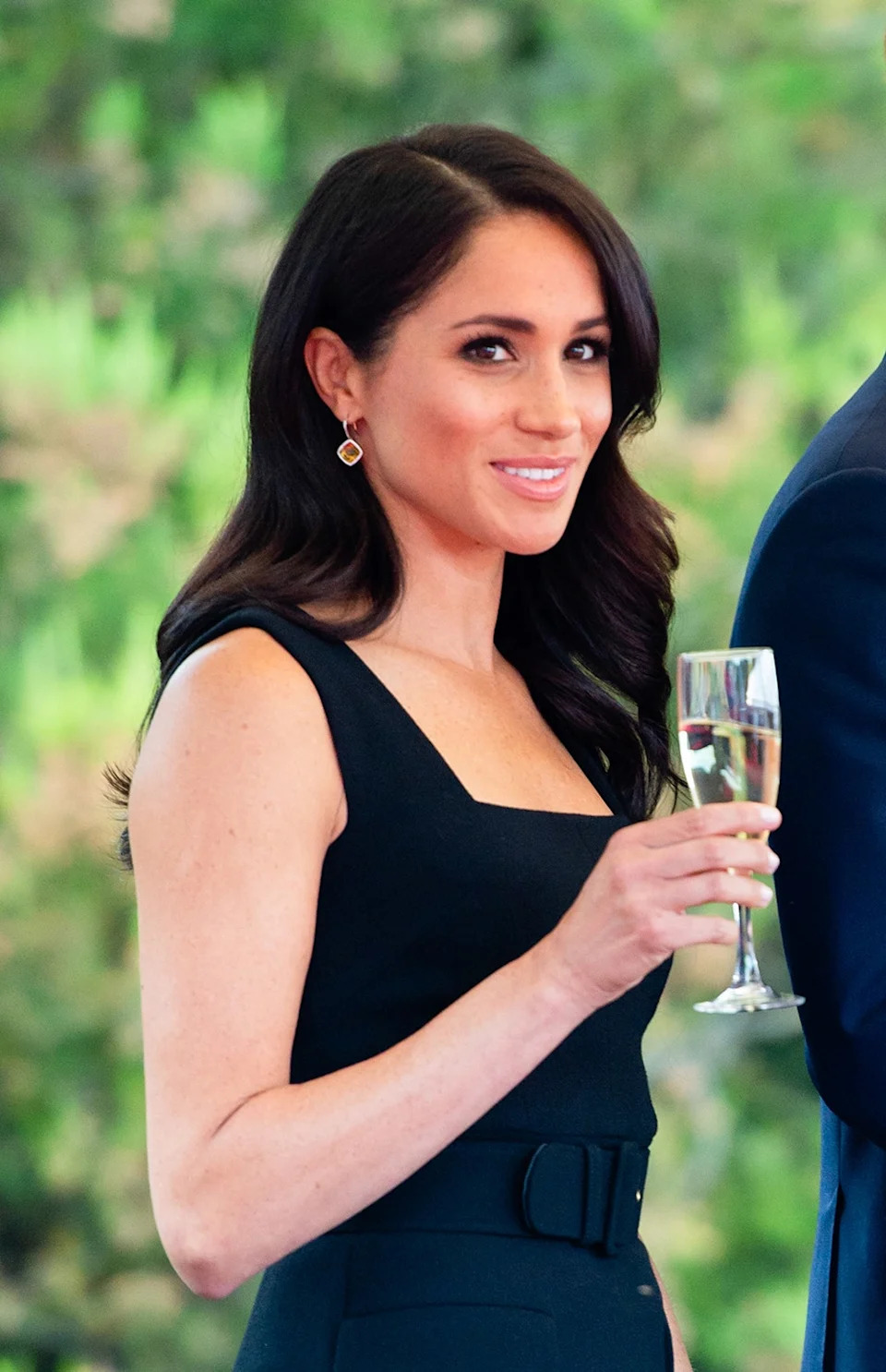 Meghan Markle wearing a strappy black dress holding a champagne flute.