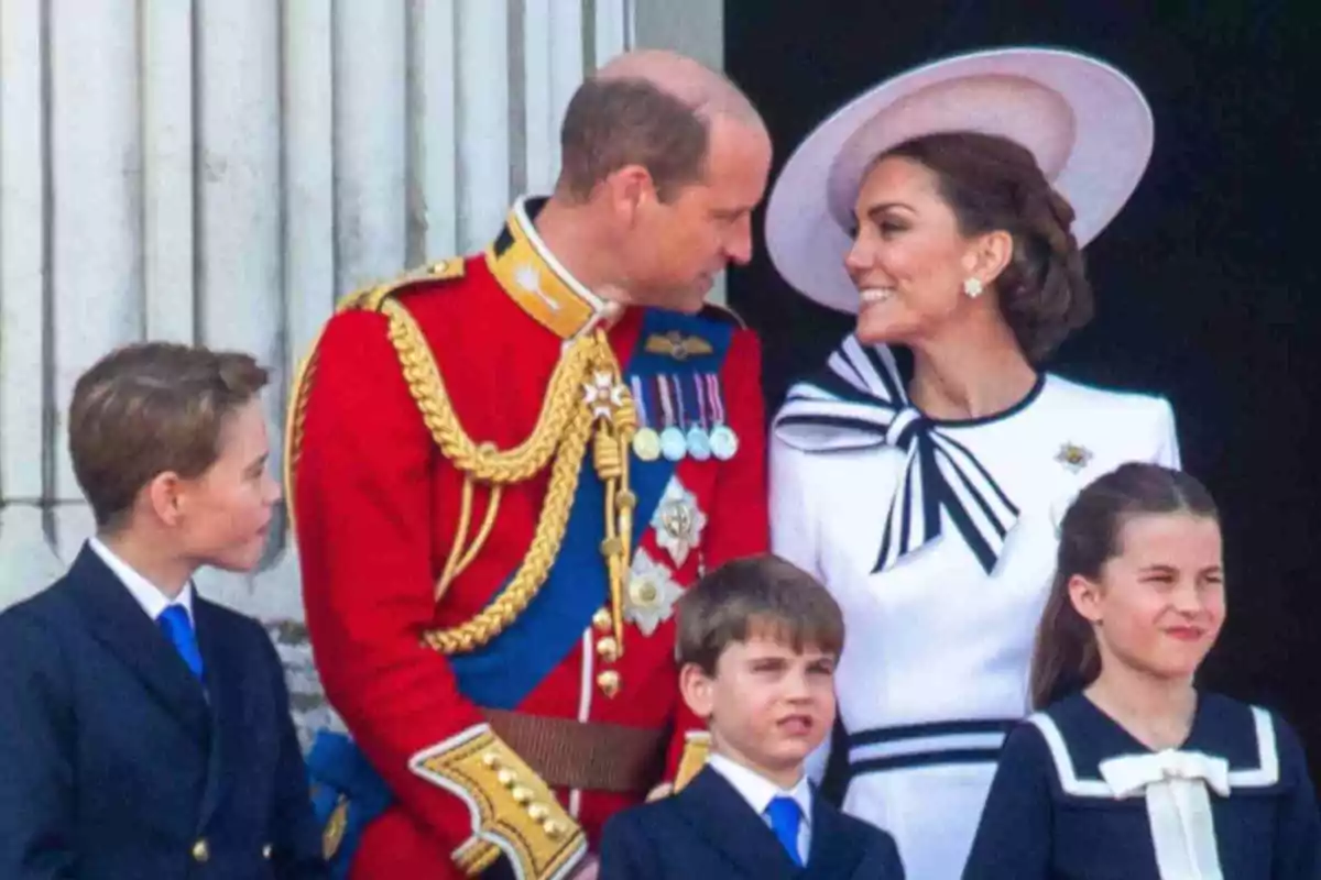 Prince William, Kate Middleton and their children George, Charlotte and Louis dressed elegantly smile while standing in front of a building with columns.