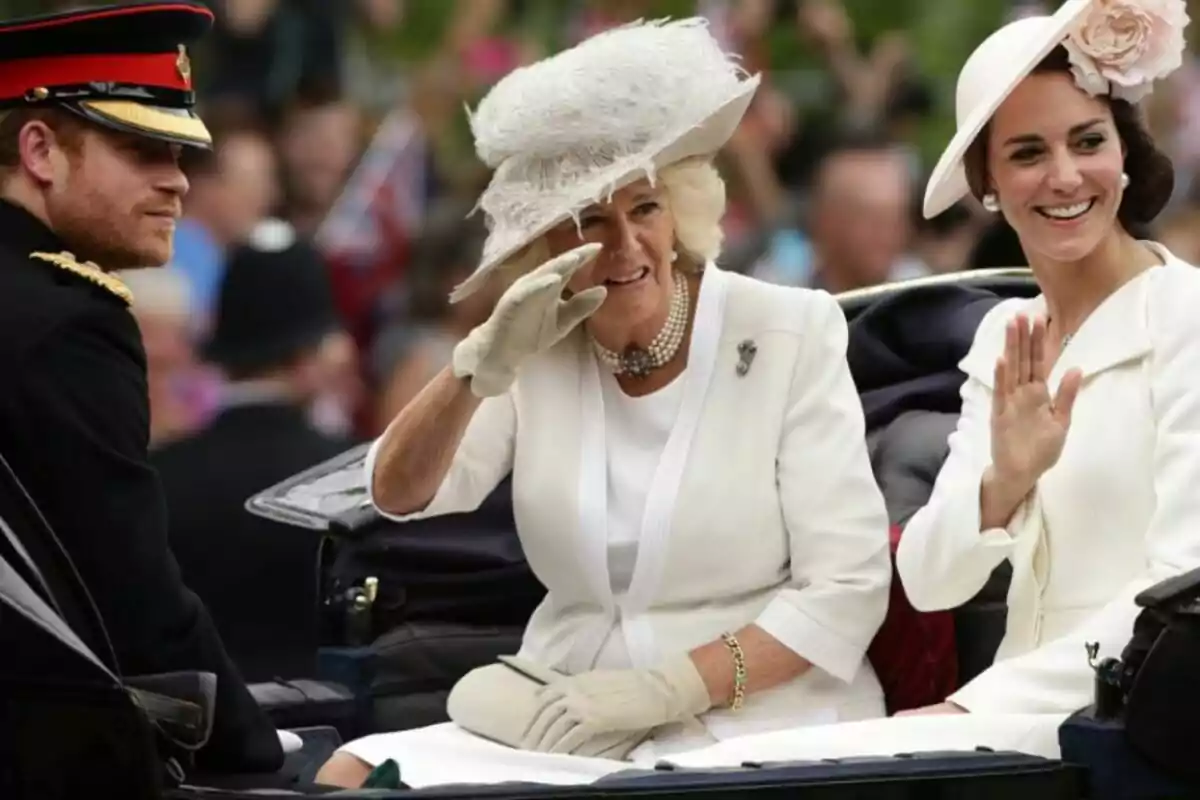 Three elegantly dressed people ride in a carriage during a public event; two of them wave and smile while the crowd watches in the background.