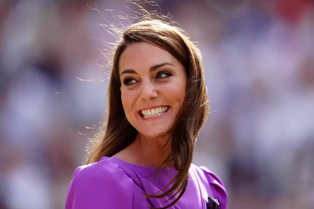 Young woman with long brown hair smiling and wearing a purple dress with a blurred background