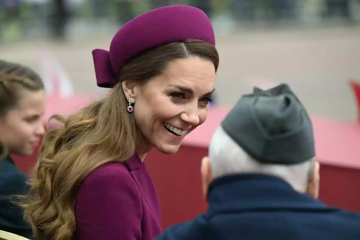 A smiling woman in a purple hat talks with an older man wearing a gray cap.