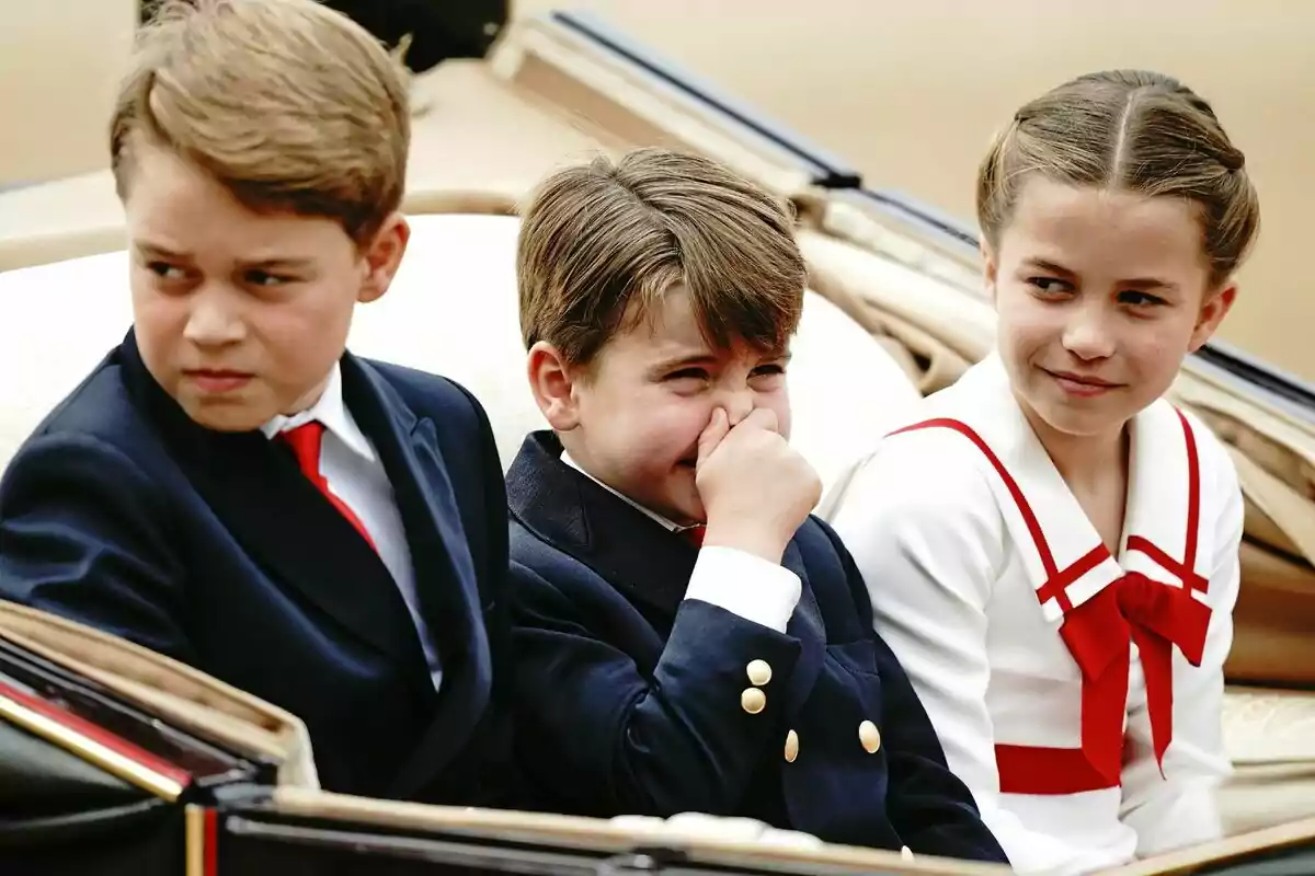 Three formally dressed children are sitting in a carriage, one of them covering his nose while the other two look in opposite directions.