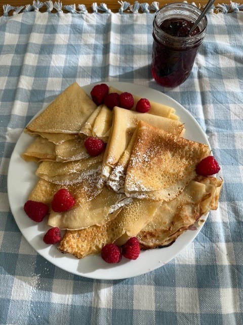 plate of crepes garnished with raspberries and powdered sugar accompanied by a jar of jam