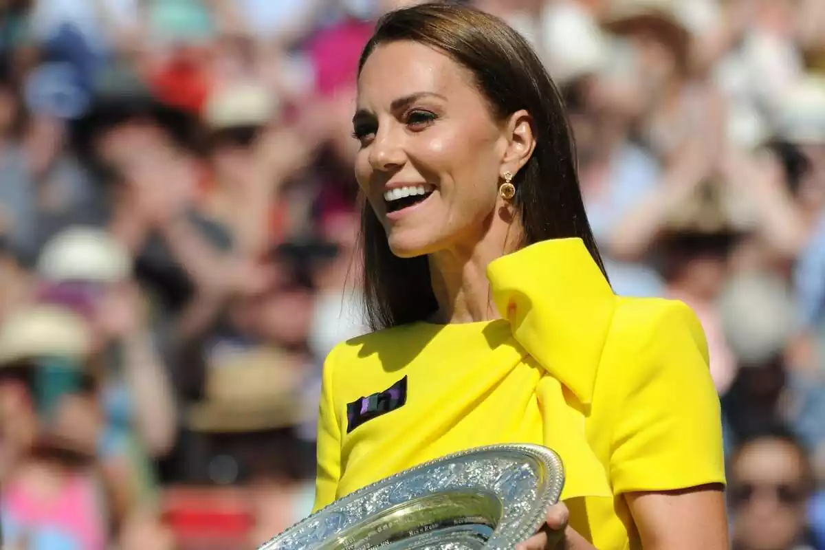 Kate Middleton laughing in a yellow dress and a silver plate in her hands