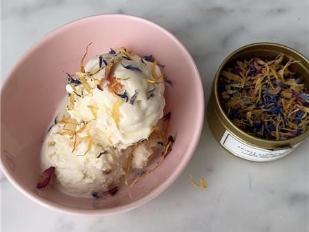 meghan markle as ever flower sprinkles scoop of ice cream topped with edible flowers in a pink bowl next to a tin of dried flowers