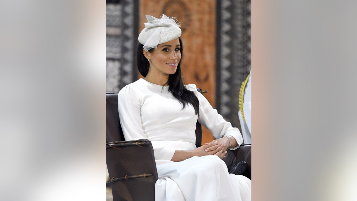 Meghan Markle wearing a white dress with a matching fascinator smiling.