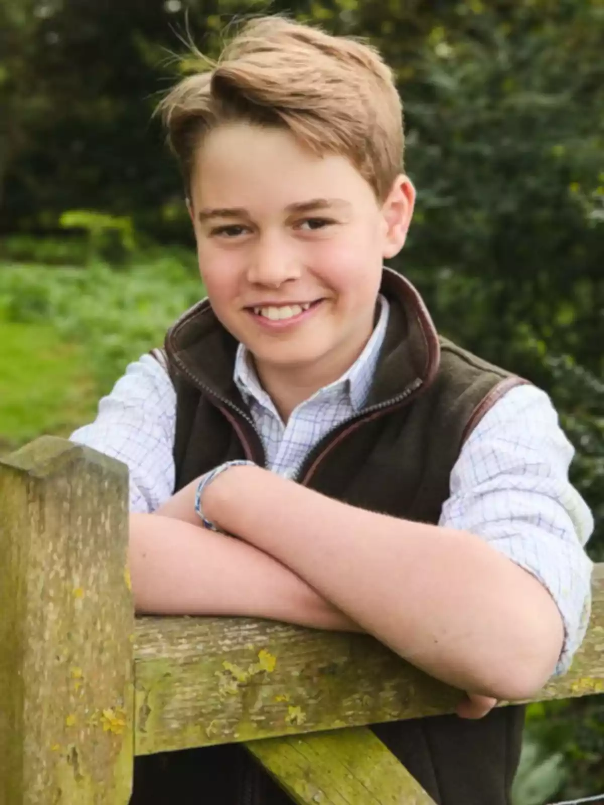 Smiling young man leaning on a wooden fence in a natural setting
