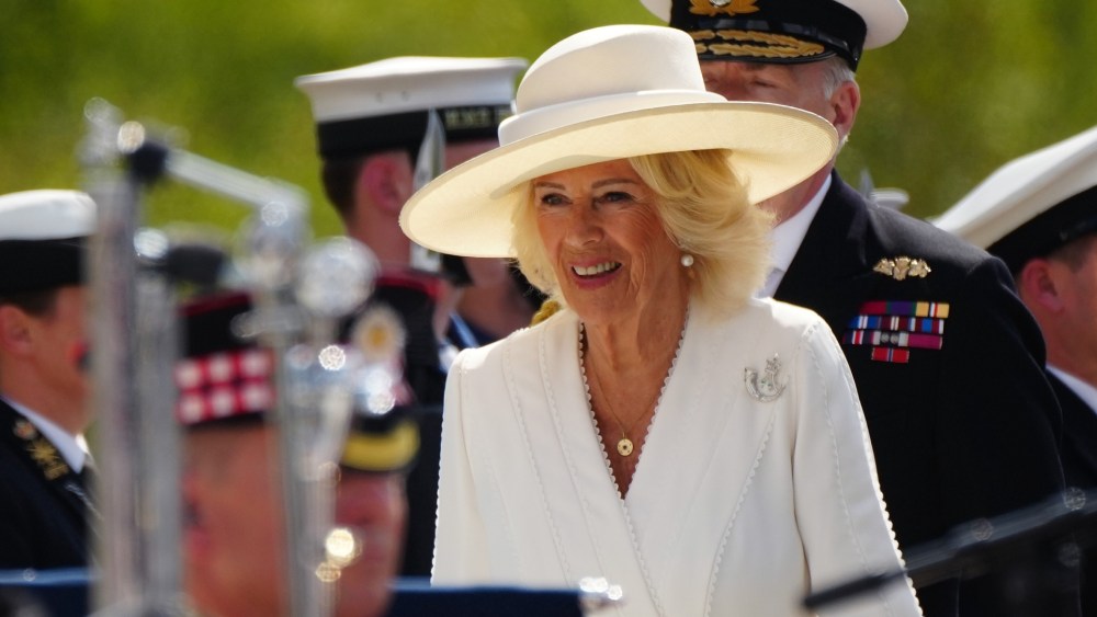 Queen Camilla wears white Dior dress and British bugle horn brooch for VJ Day celebration.