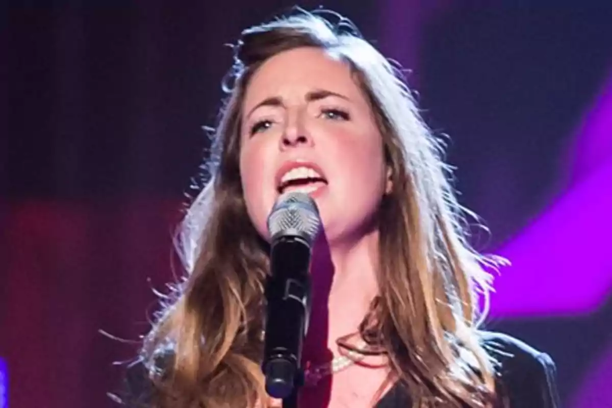 Rose Farquhar singing on stage with a microphone in her hand and colorful lights in the background
