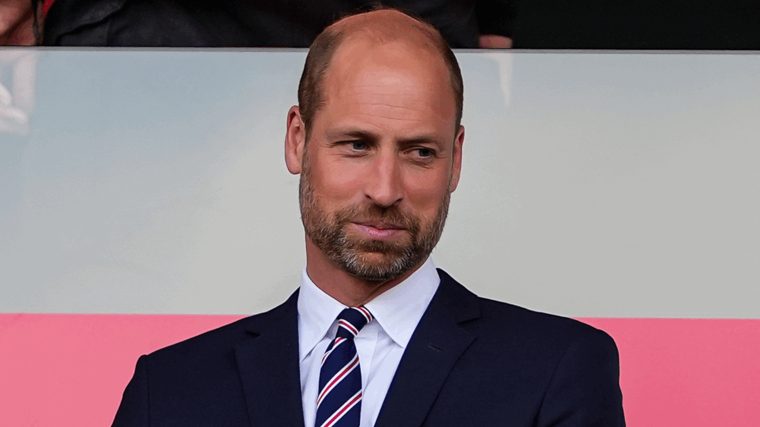 Prince William’s Favorite Hobby Is Definitely Unexpected Prince William wearing a suit and tie in front of a pink and white background
