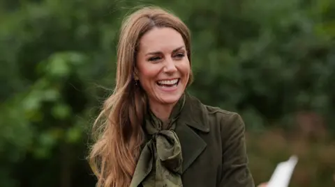 Yui Mok/PA Wire The Princess of Wales wearing a green silk scarf and a green jacket. She is laughing with a big smile on her face. 