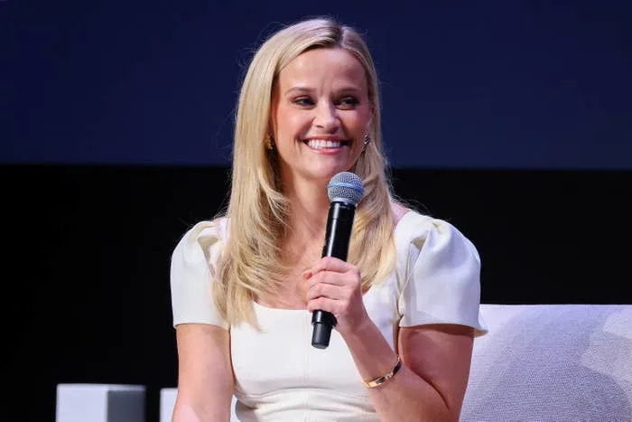 Actress in a cap-sleeve dress smiling while holding a microphone on stage
