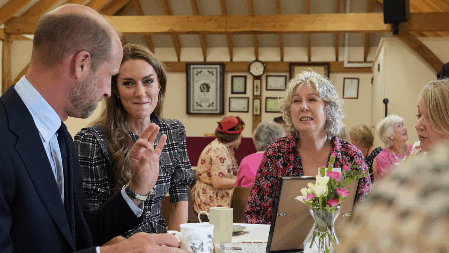Prince William wearing a suit sitting with Princess Kate at a table full of cakes and tea