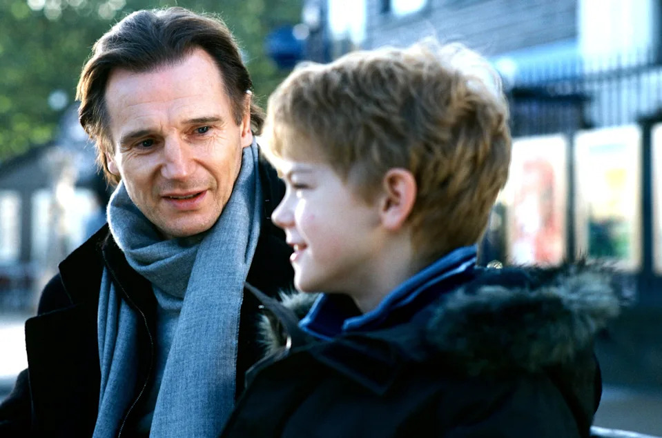 An adult and a child share a conversation outdoors. The adult wears a scarf and coat