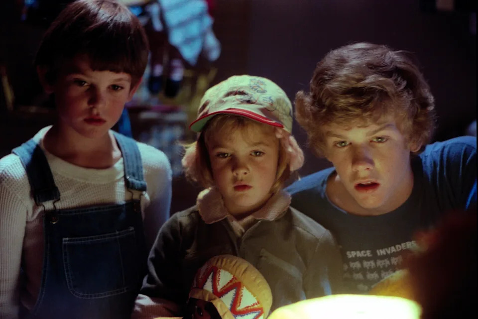 Three children intently gaze at a glowing object, creating a sense of wonder, in a scene evoking classic 80s adventure films