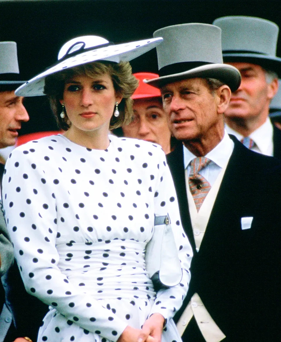 Princess Diana looking on with a serious look on her face as Prince Philip speaks to her in the U.K.
