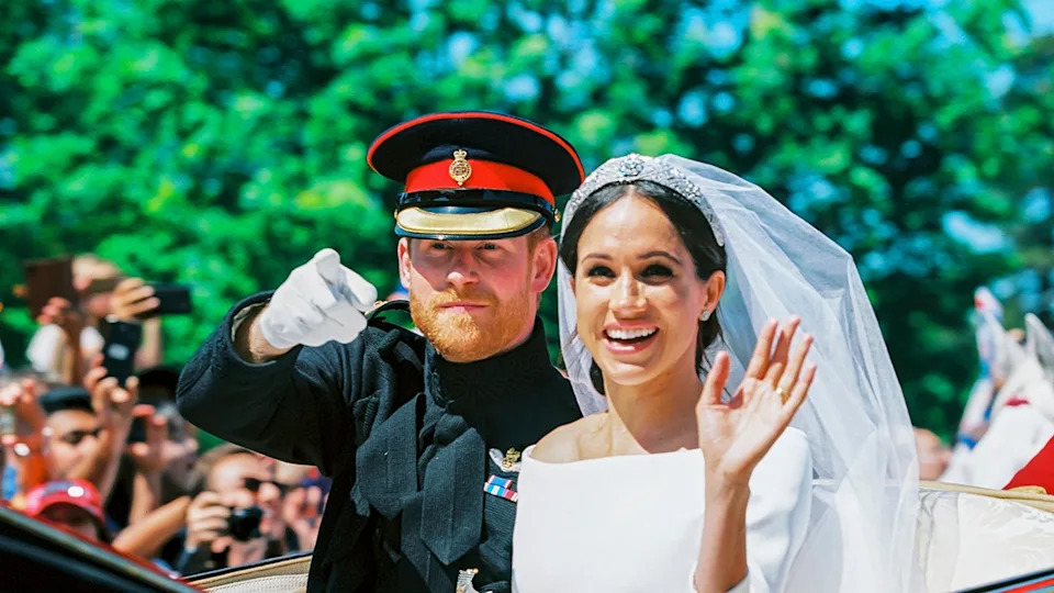 Prince Harry pointing in his suit as Meghan Markle waves on their wedding day in 2018.