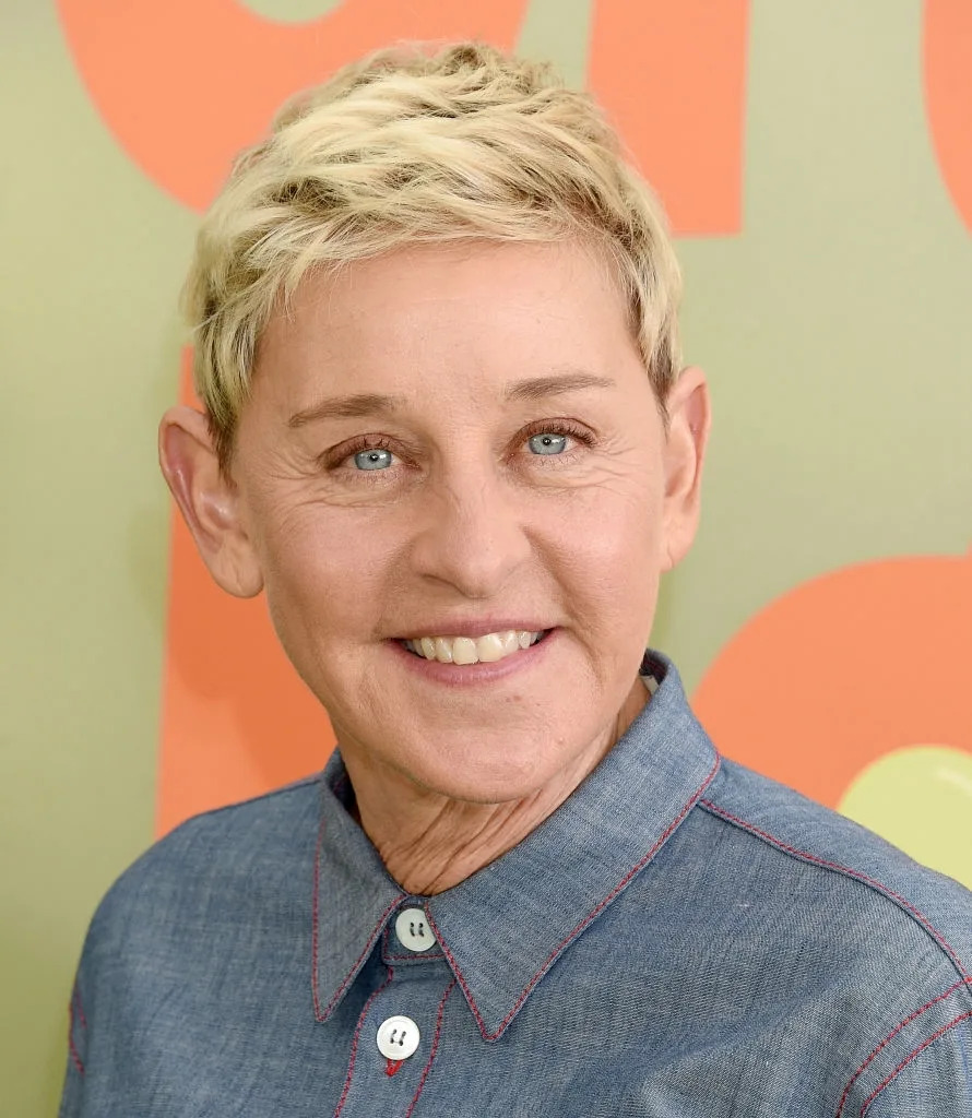 Person with short hair smiling, wearing a collared denim-style shirt