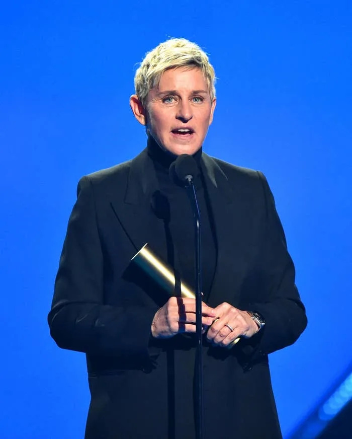 Person in a black suit holding an award and speaking into a microphone on stage