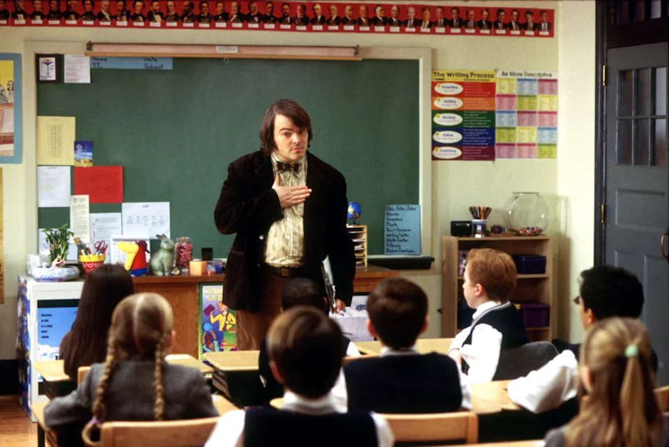A teacher passionately addresses students in a classroom filled with educational posters and a green chalkboard