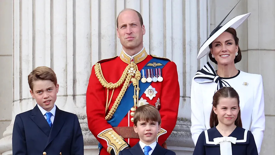 Prince William and Kate Middleton in formal wear standing on the balcony of Buckingham Palace with their three young children.