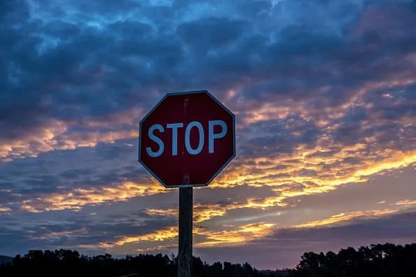 A stop sign stands against a backdrop of a dramatic, cloudy sky during sunset