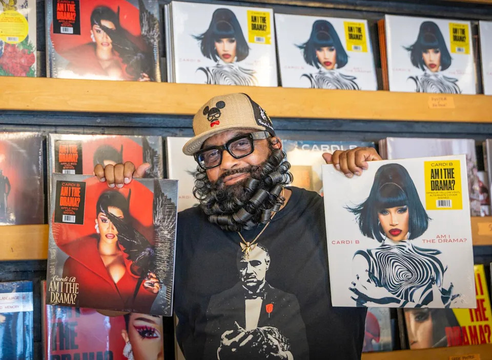 A bearded man holds Cardi B albums in a record store.
