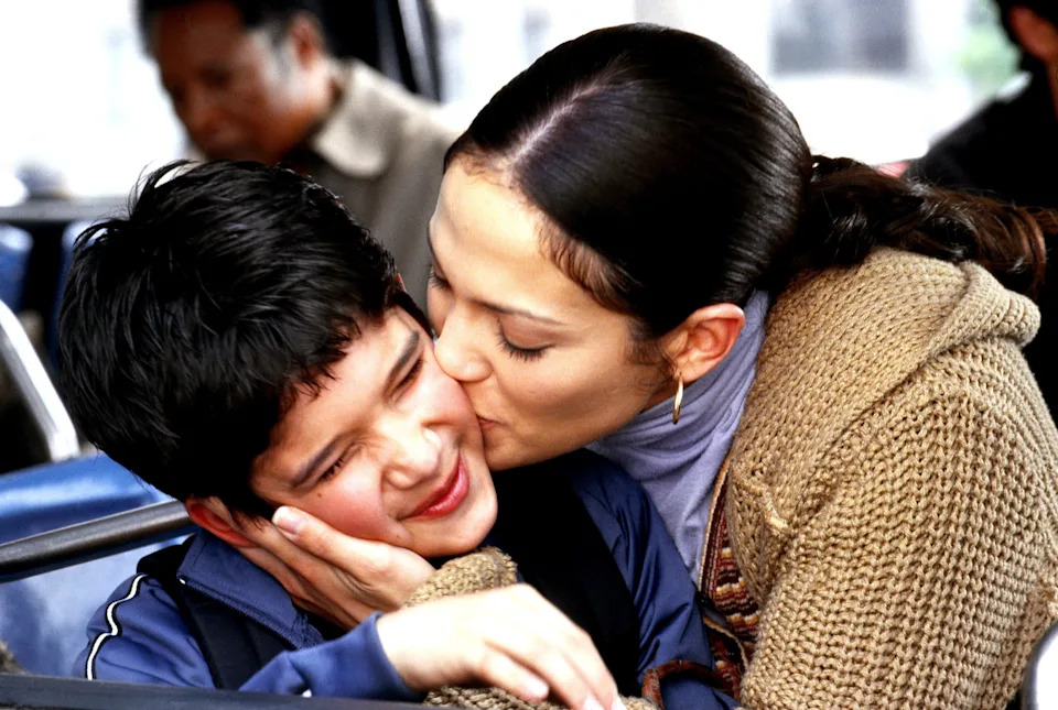 A woman gently kisses a young boy on the cheek inside a bus. They share a warm, affectionate moment