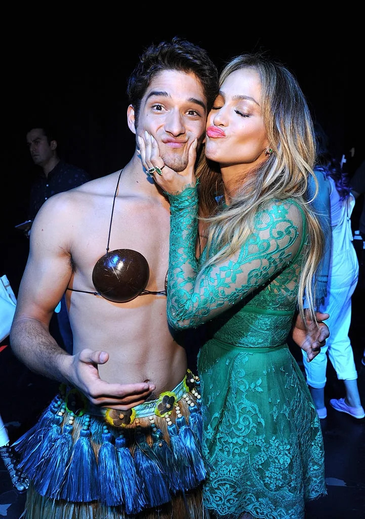 Two people embrace playfully; one wears a hula skirt and coconut top, while the other is in a lace dress, posing affectionately for the camera