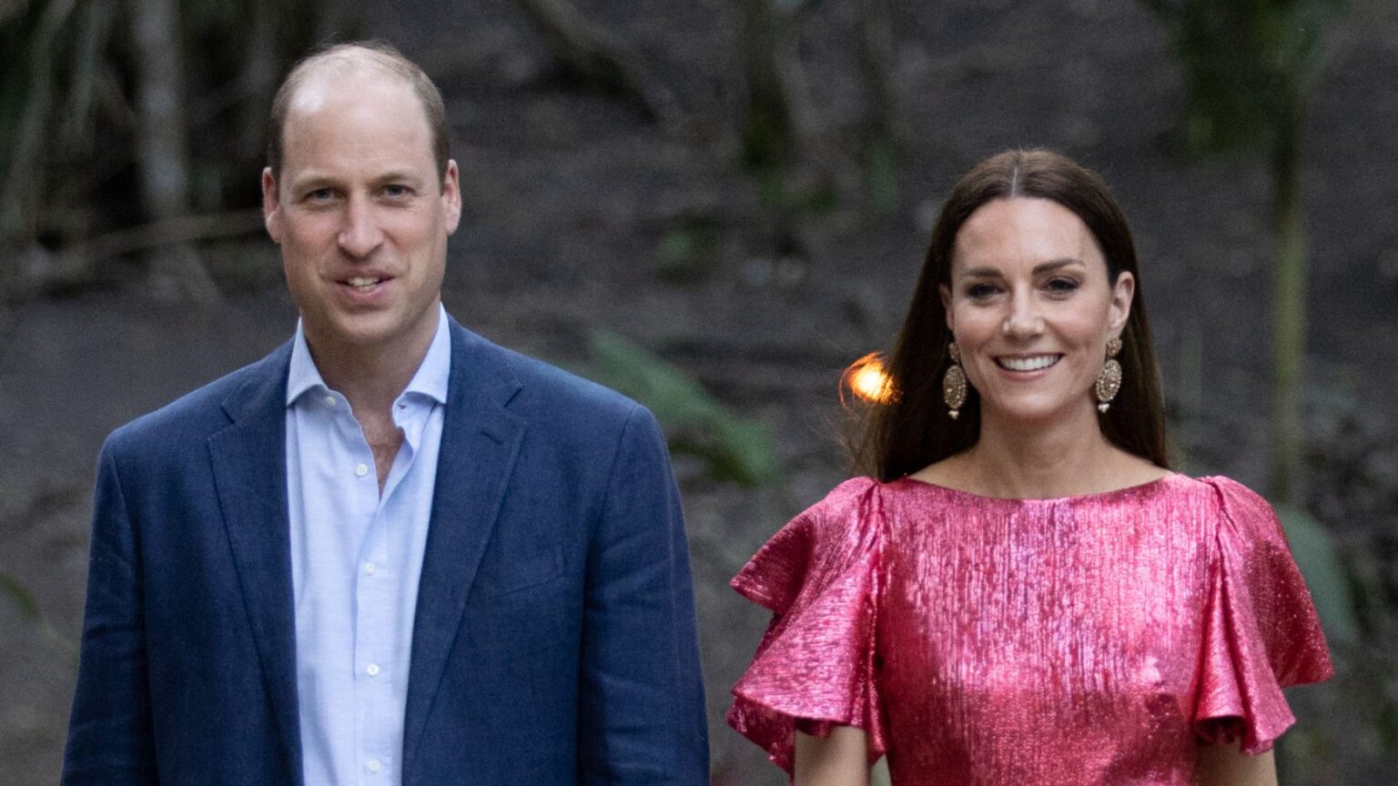 Prince William wears a navy suit with a light blue shirt and Kate Middleton wears a metallic pink dress