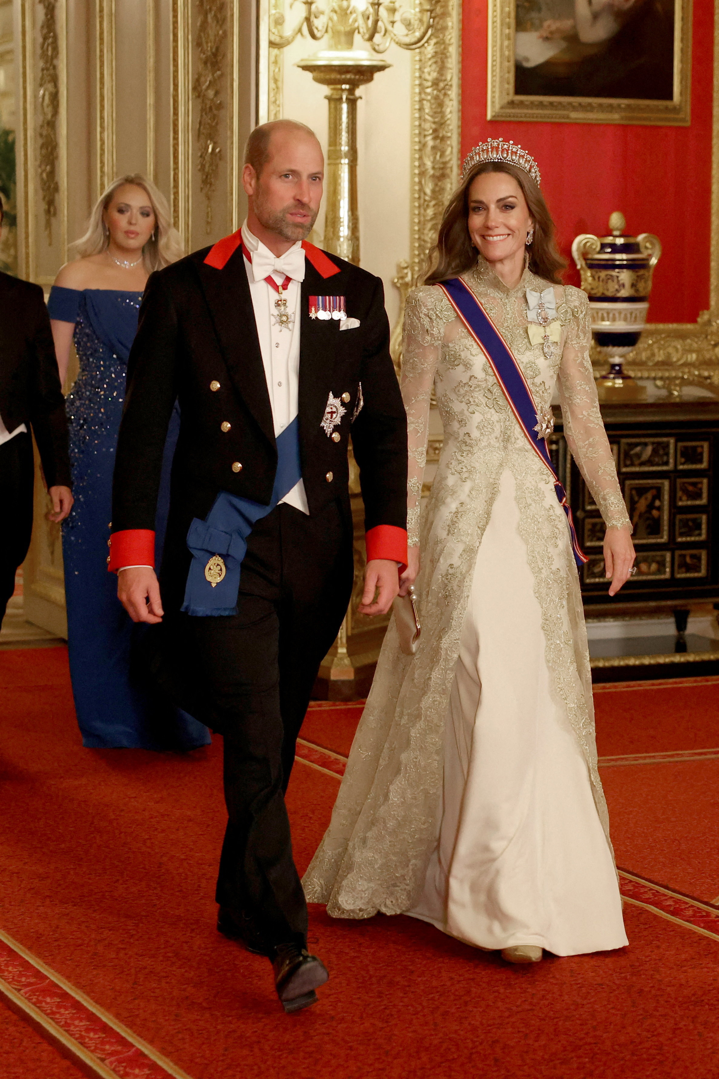 Kate Middleton and Prince William walking into a banquet wearing a gold gown and a black suit