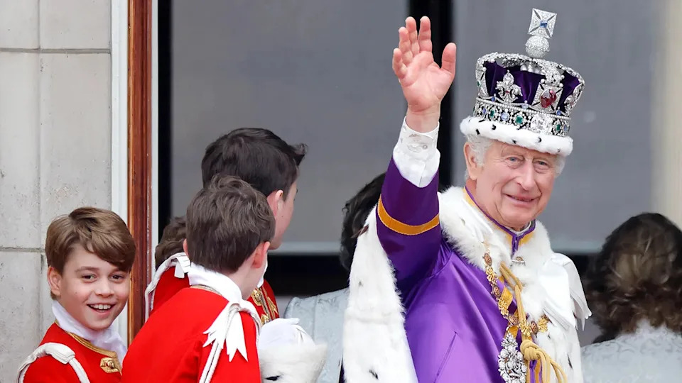 King Charles in a royal robe and crown waving as Prince George smiles on.