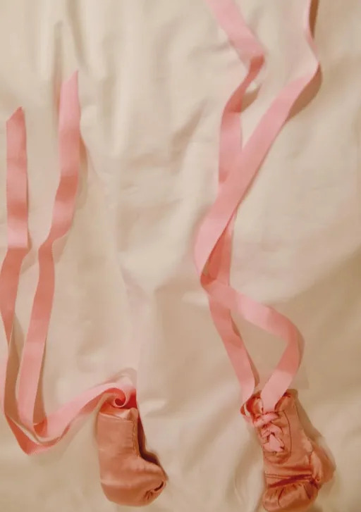 Ballet pointe shoes with long ribbons displayed on a surface