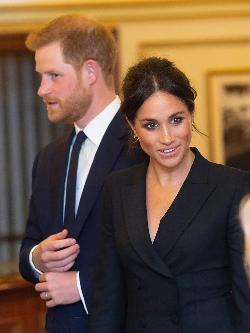 Meghan Markle speaking to someone as Prince Harry looks on.