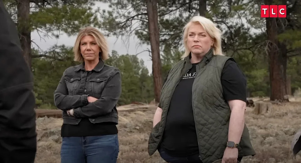 Meri Brown and Janelle Brown stand with serious expressions during an outdoor scene on Sister Wives, surrounded by trees.