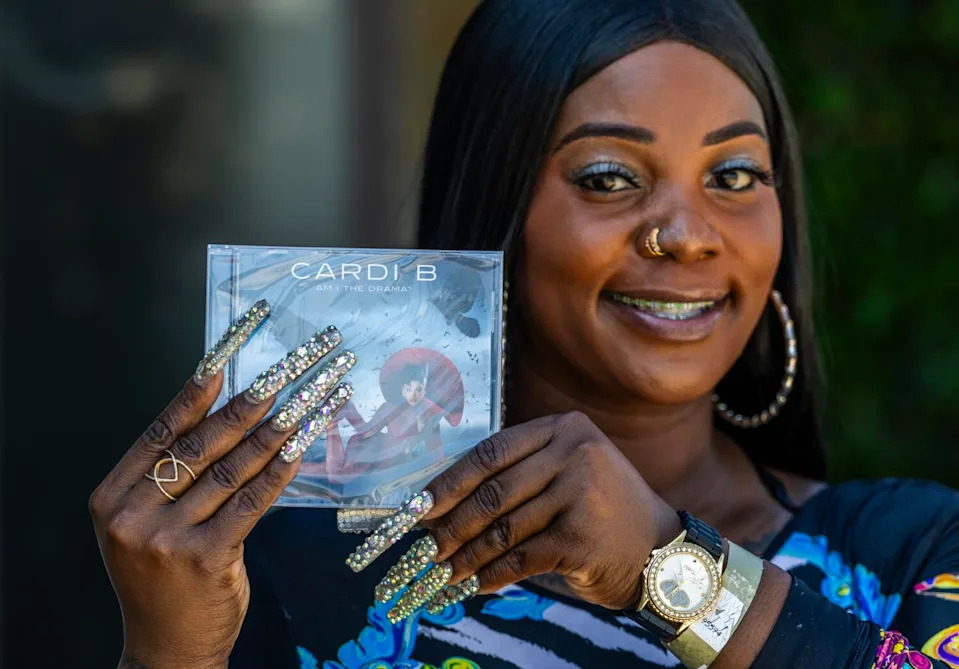 A smiling woman holds a Cardi B CD.