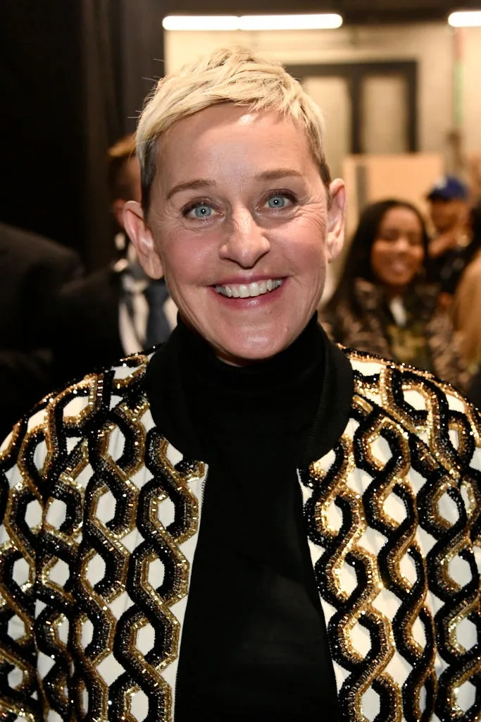 Person smiling in a geometric-patterned jacket over a black shirt at an indoor event