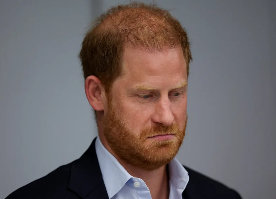 Prince Harry with a beard and serious expression is looking down, wearing a suit and collared shirt