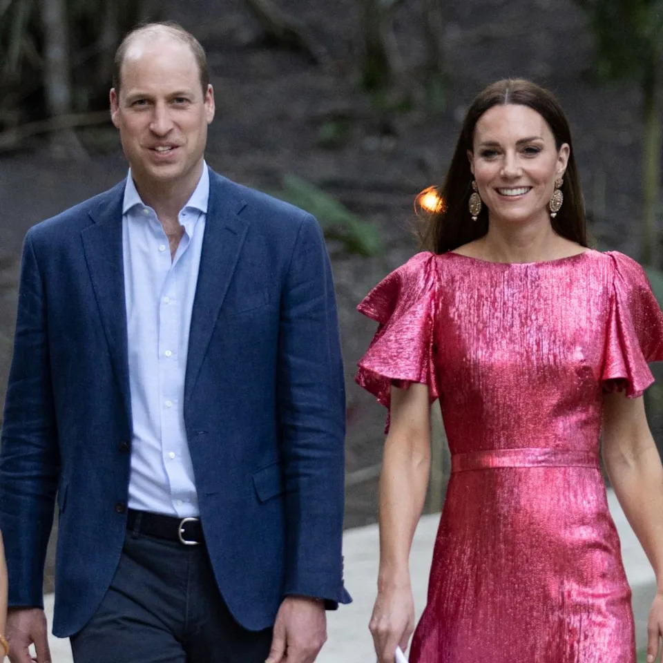  Prince William wears a navy suit with a light blue shirt and Kate Middleton wears a metallic pink dress. 