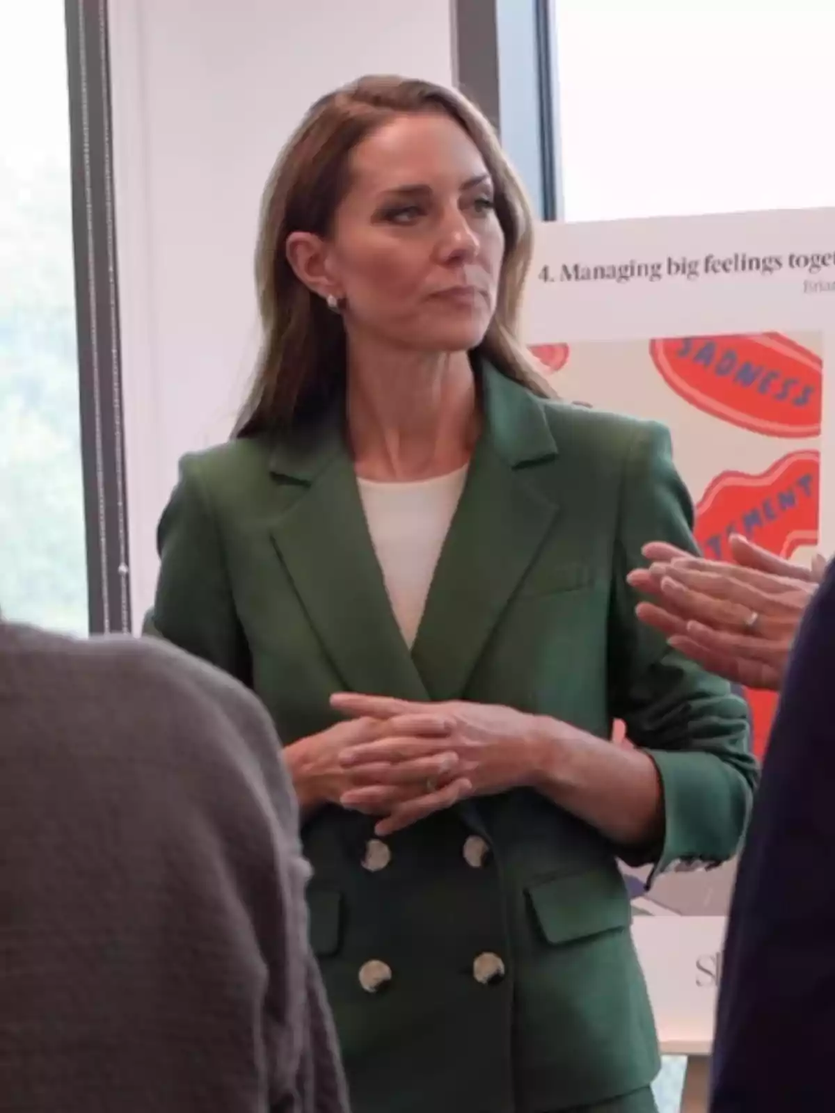 Brown-haired woman in a green blazer listening alertly during a conversation in a professional setting