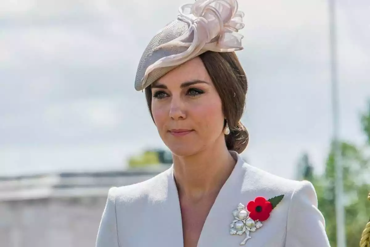 Kate Middleton serious with a beige headdress, her hair up and a pin with a flower