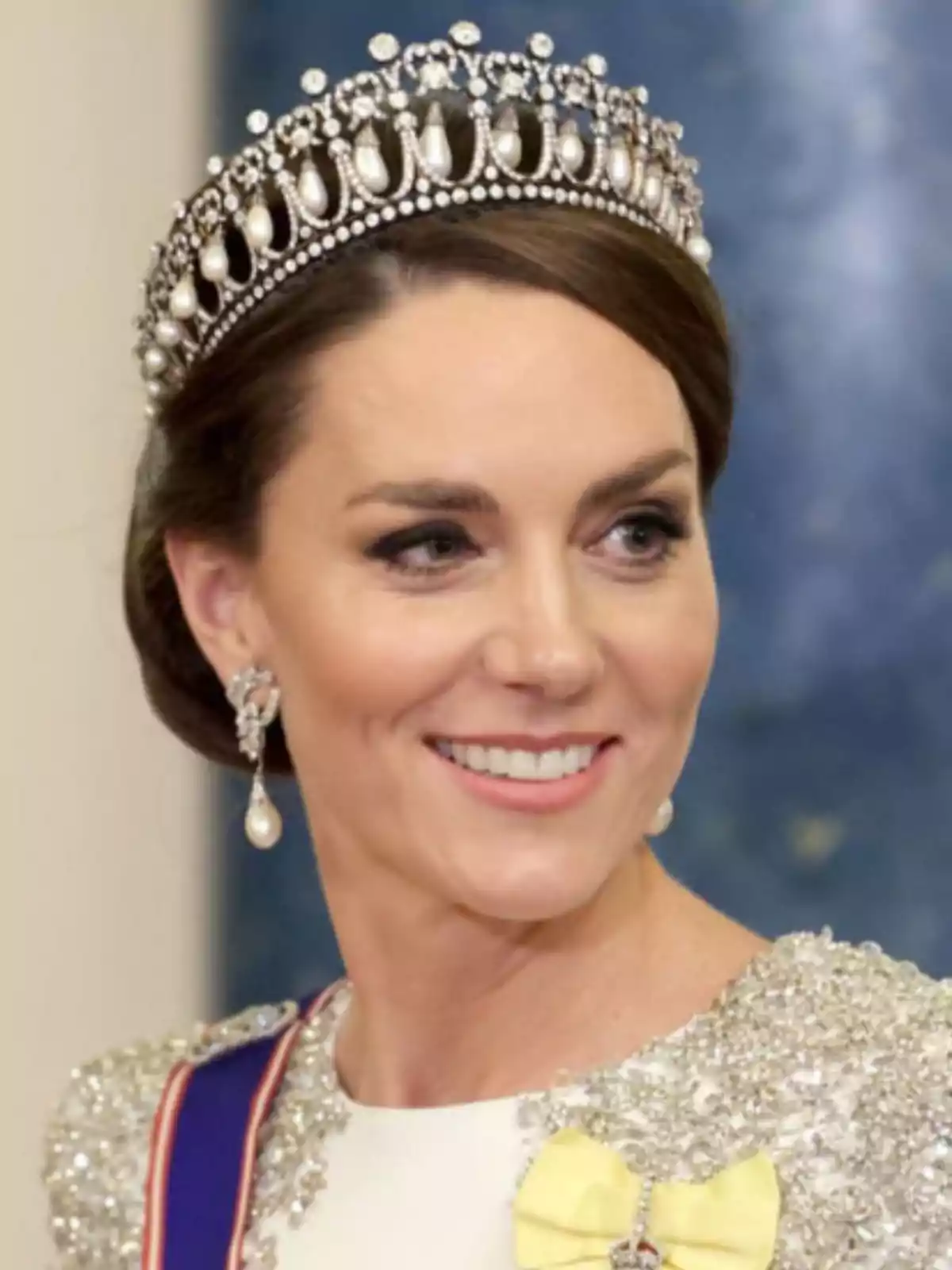 Smiling woman with a pearl and diamond tiara, elegant dress with sparkling details, and a yellow bow