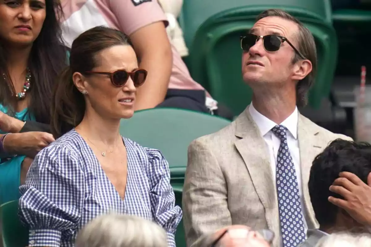 People sitting at an outdoor sporting event, wearing sunglasses and looking up.