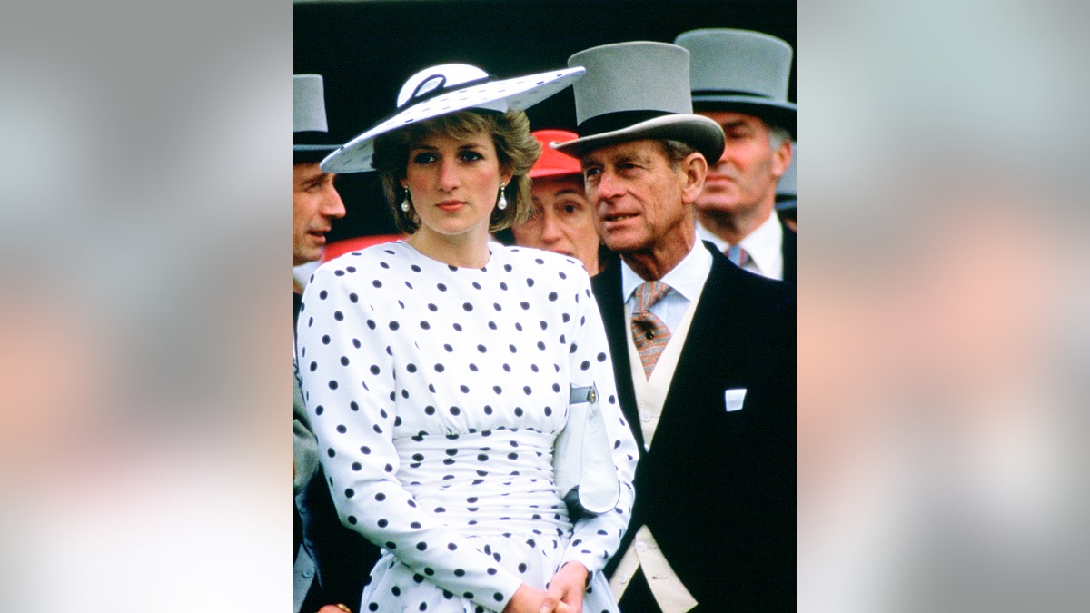 Princess Diana looking on with a serious look on her face as Prince Philip speaks to her in the U.K.
