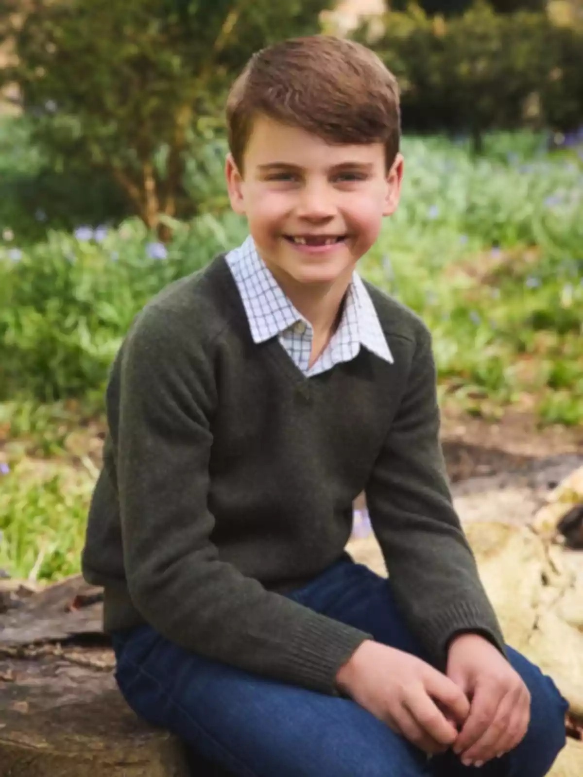 Smiling boy sitting outdoors wearing a green sweater and a plaid jersey in a natural setting Smiling boy sitting outdoors wearing a green sweater and a plaid jersey in a natural setting