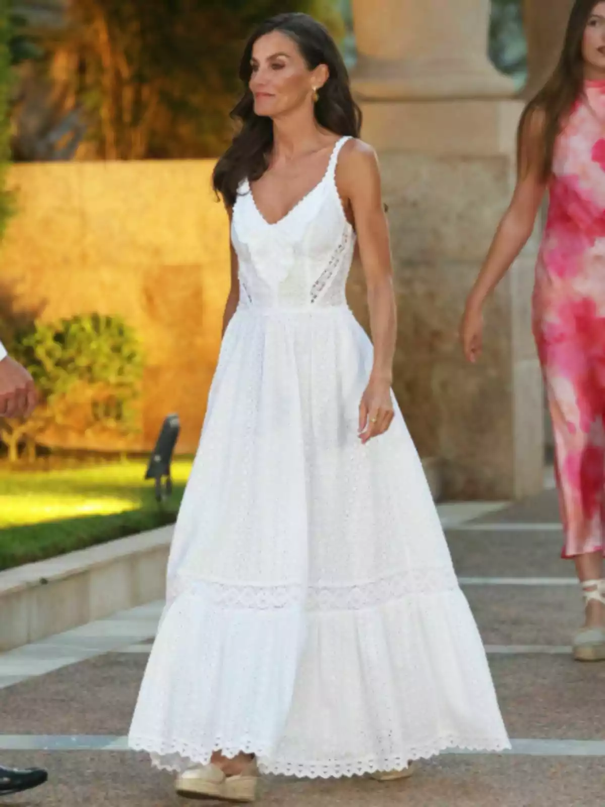 Queen Letizia in a long white strappy dress and beige sandals walking outdoors